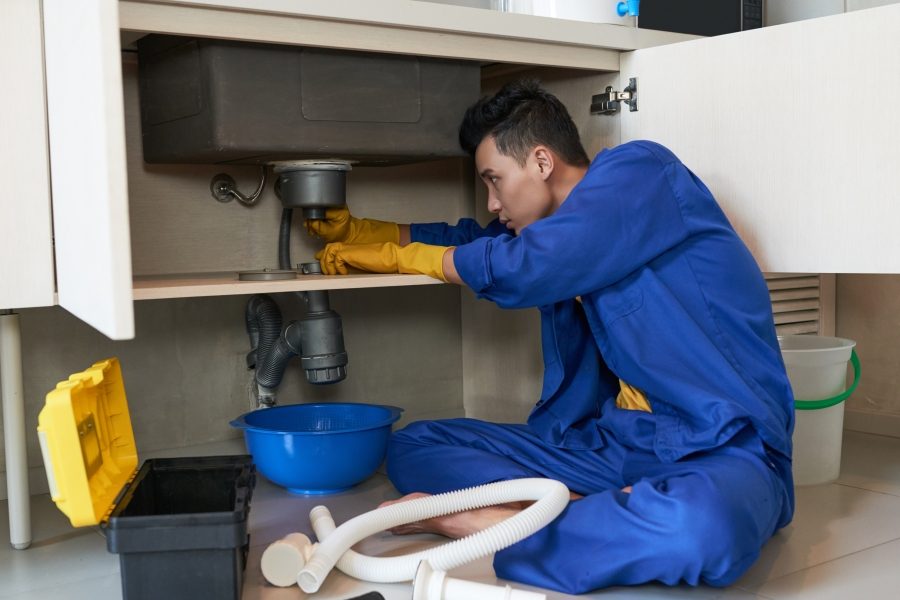 Young Vietnamese plumber checking drain in kitchen